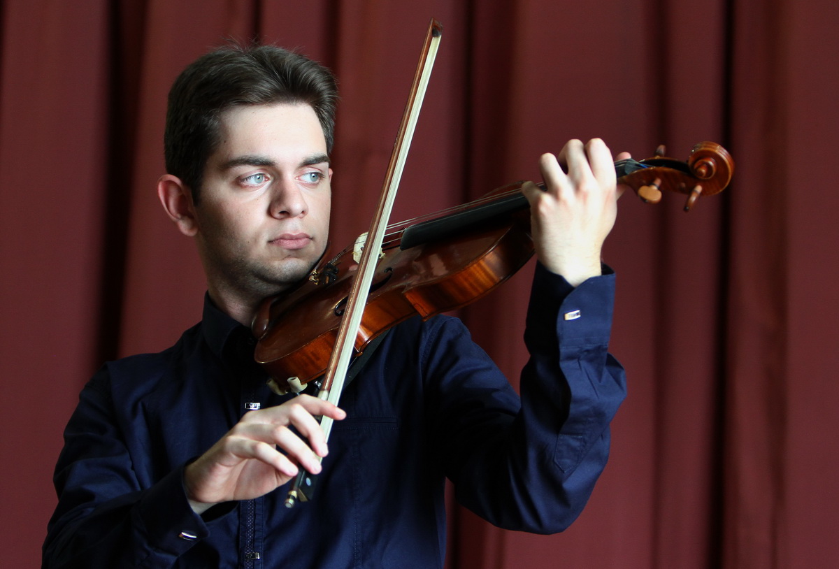 David Kurtic playing violin in front of a red curtain